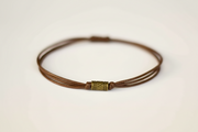 Brown leather cord bracelet with a metal clasp on a light beige background