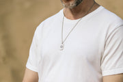 Person wearing a white t-shirt and a necklace with a dog tag against a blurred background