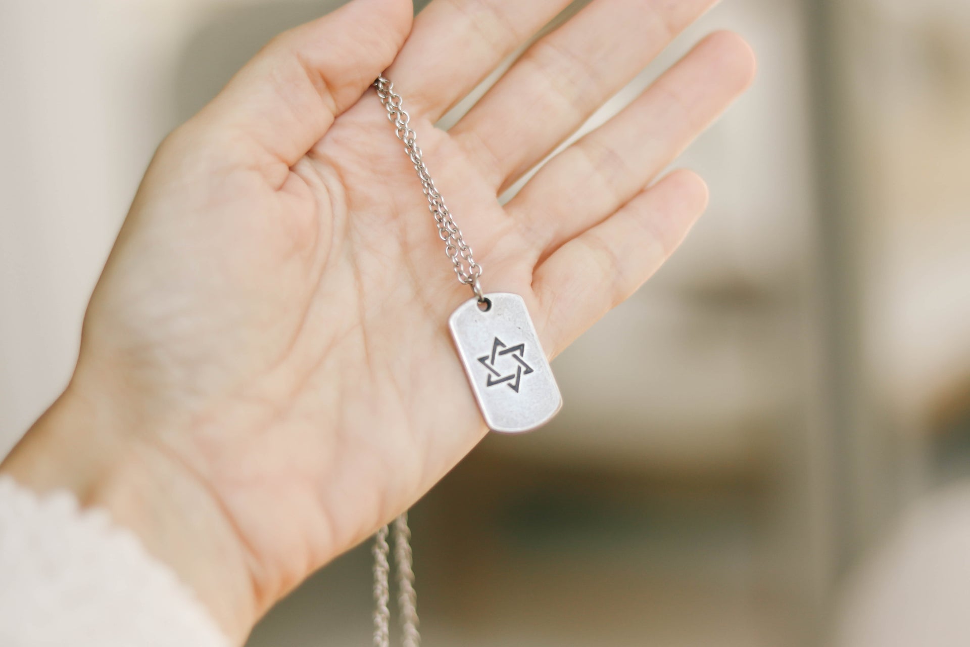Hand holding a silver dog tag with a star emblem against a blurred background