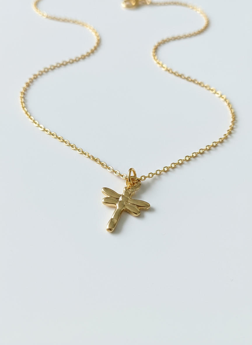 Gold necklace with a dragonfly pendant on a light gray background