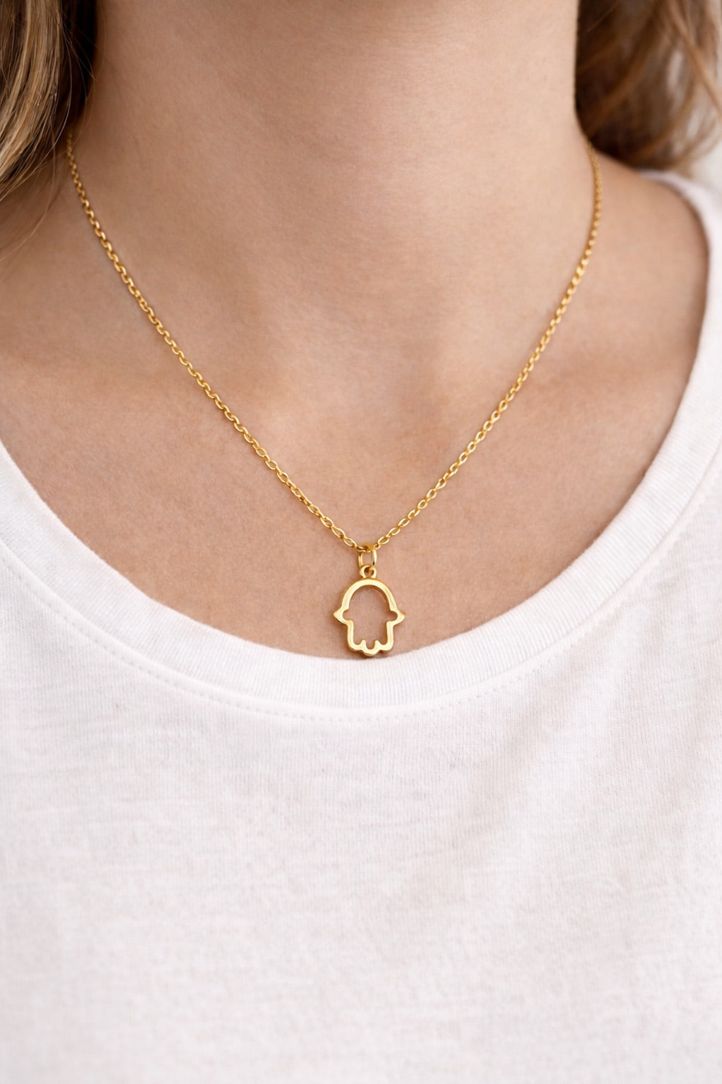 Gold necklace with a hamsa hand pendant on a white background