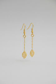 Gold earrings with leaf designs on a light gray background