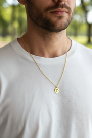 Man wearing a gold necklace with a small om round pendant outdoors