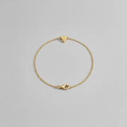 Gold bracelet with a triangle-shaped clasp on a light gray background