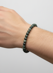 Green beaded bracelet Kambaba Jasper stone on a wrist against a light gray background