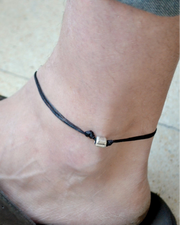 Ankle with a black cord anklet featuring a silver clasp on a light background