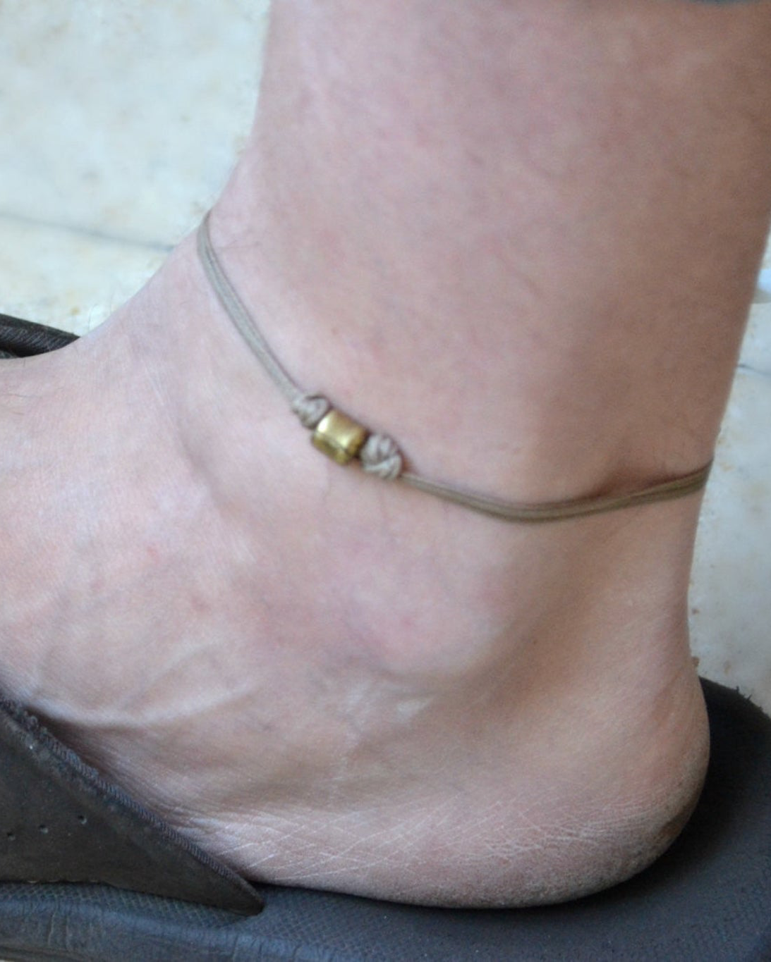 Close-up of a foot wearing a anklet with a small charm on a light background