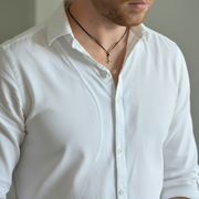 Man wearing a white shirt with an anchor necklace against a neutral background