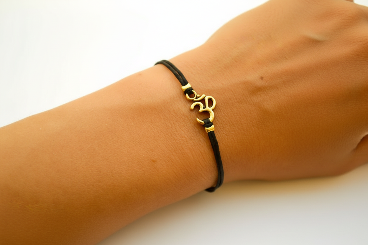 Black bracelet with a gold Om symbol on a wrist against a white background