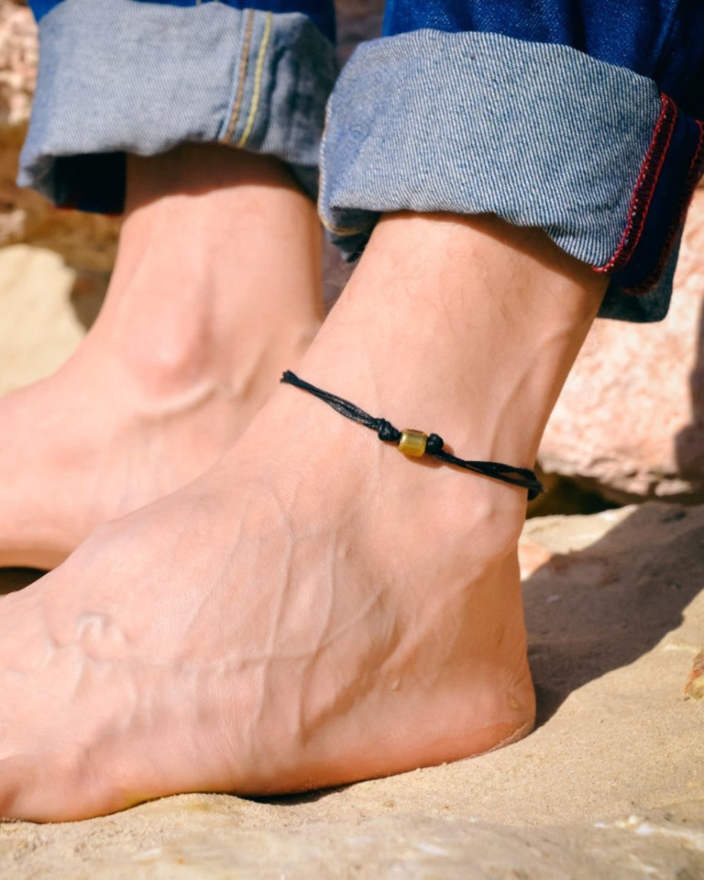 man wearing a black anklet on a rocky surface