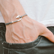 Hand wearing a silver bracelet with a fish hook charm on a plain background