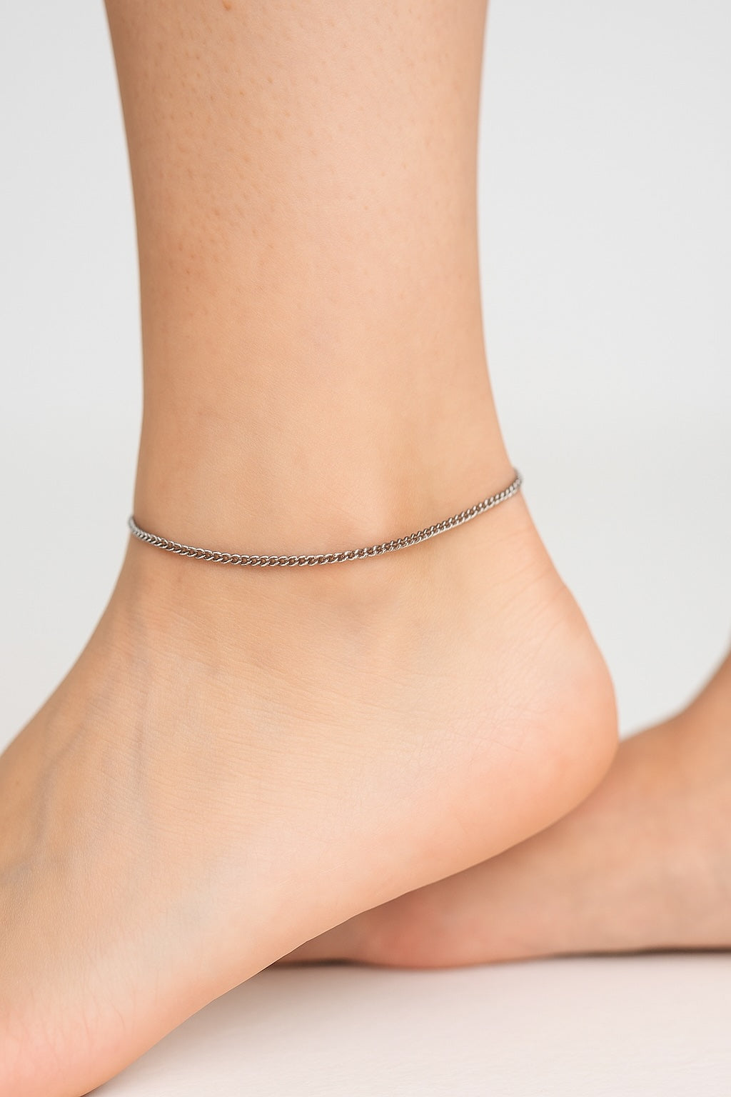 Silver anklet on a person's ankle against a neutral background
