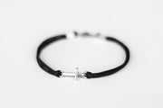 Black cord cross bracelet with a silver clasp on a light gray background