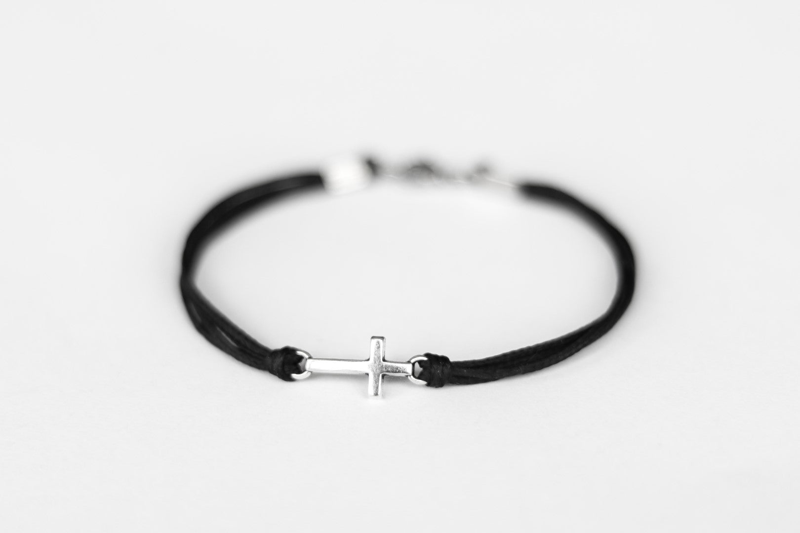 Black cord cross bracelet with a silver clasp on a light gray background