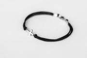 Black string cross bracelet with a silver clasp on a light gray background