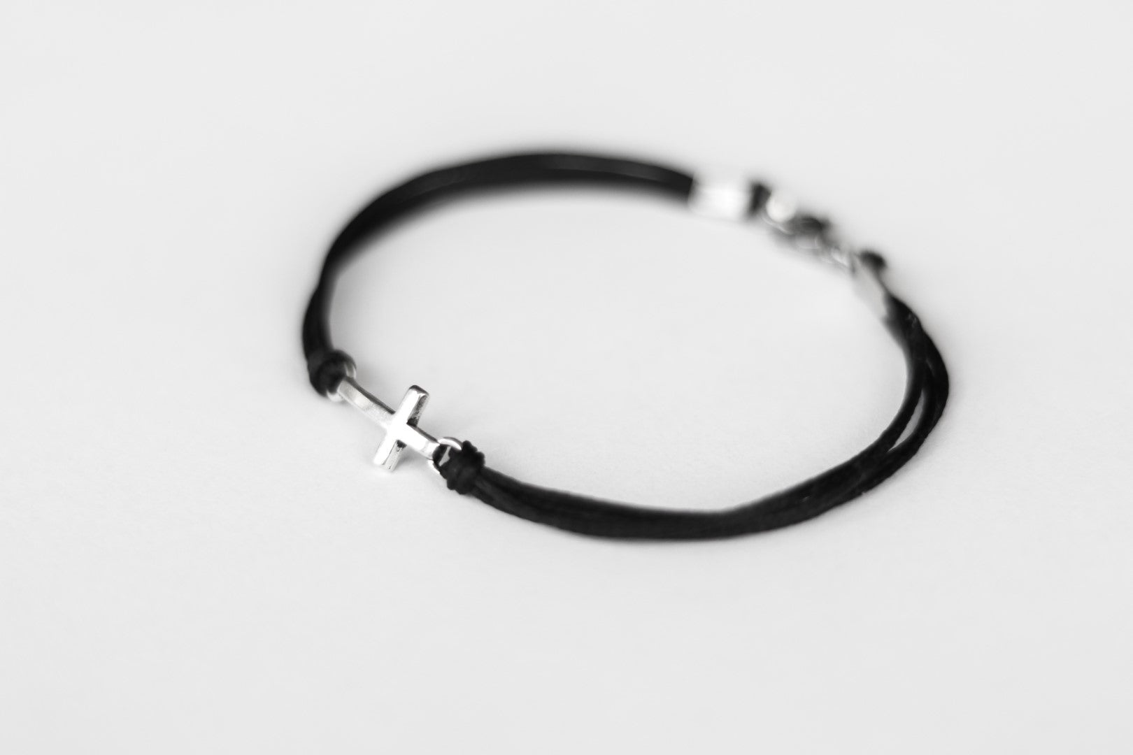 Black string cross bracelet with a silver clasp on a light gray background