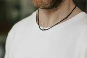 Person wearing a black necklace with a small peace pendant on a blurred background