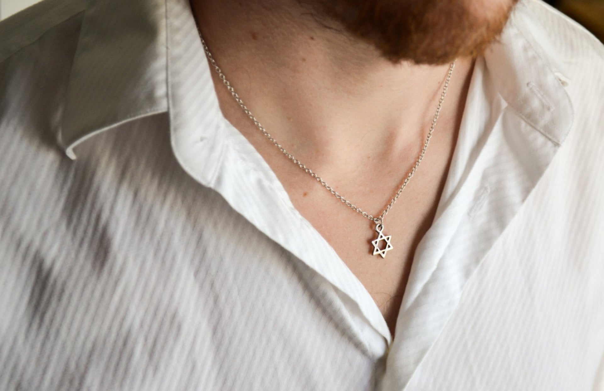 Person wearing a white shirt with a necklace featuring a Star of David pendant.