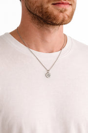 Man wearing a silver chain necklace with a sun pendant on a white background