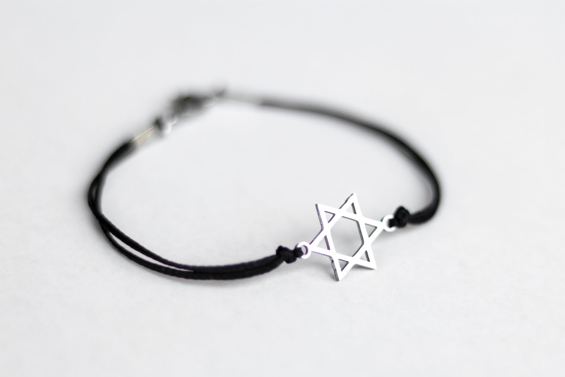 Black bracelet with a silver Star of David charm on a light gray background