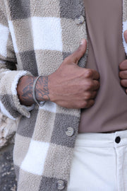 A man wearing a silver and brown checkered jacket, silver tone link chain wrapped bracelet, and light pants.