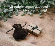 Brown velvet pouch and wrapped gift on a wooden surface with greenery in the background. Gift wrapped Jewelry
