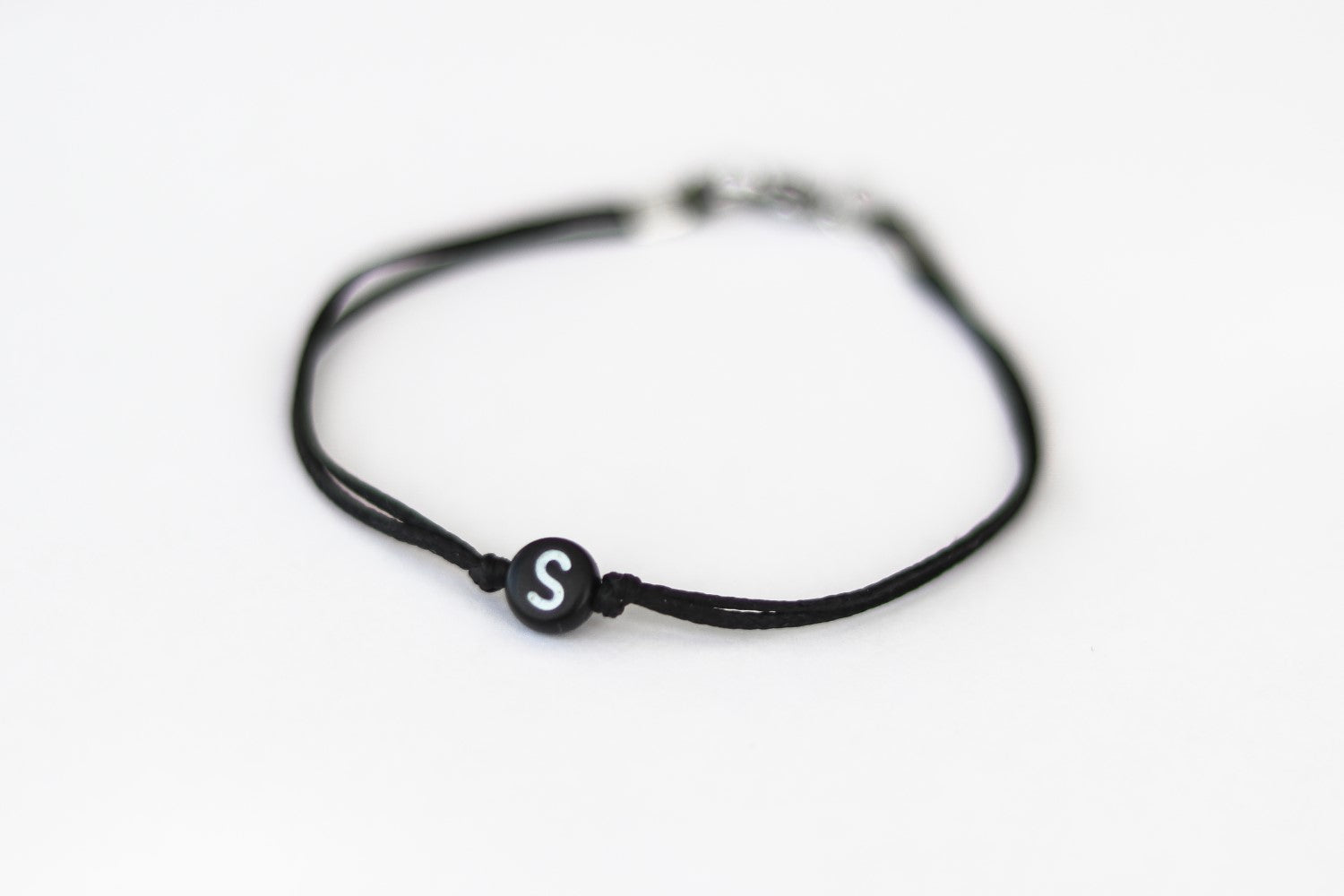 A man's wrist wearing a black cord bracelet with a black round bead and a initial letter